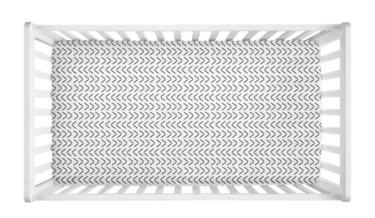White crib sheet with black mudcloth-style arrow pattern in a modern white crib.