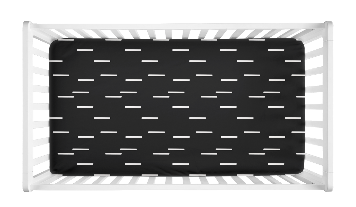 Black crib sheet with minimalist white mudcloth dash pattern shown in a modern white crib.