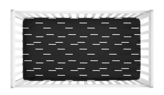 Black crib sheet with minimalist white mudcloth dash pattern shown in a modern white crib.