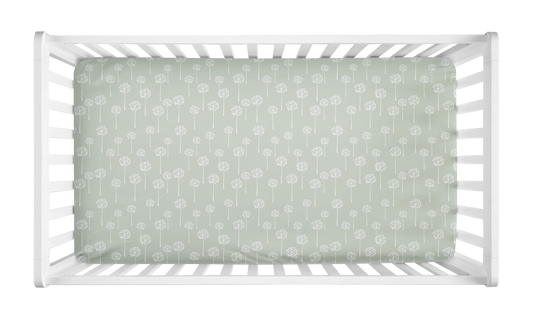 Crib sheet with sage green background and white dandelion print, styled in a white crib for a botanical or minimalist baby girl nursery