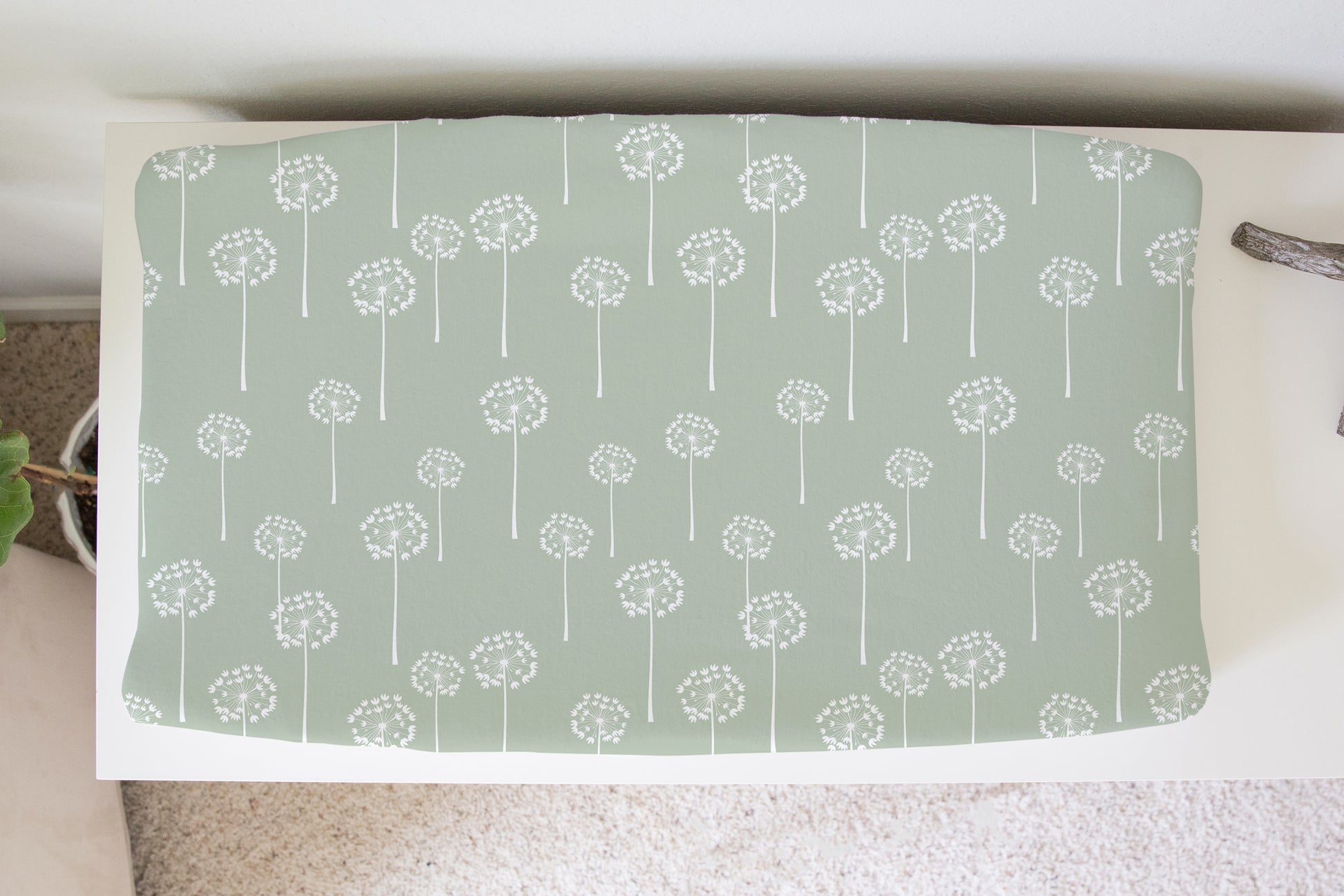 Sage green changing pad cover with white dandelion print styled on a white changing table