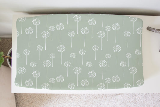 Sage green changing pad cover with white dandelion print styled on a white changing table