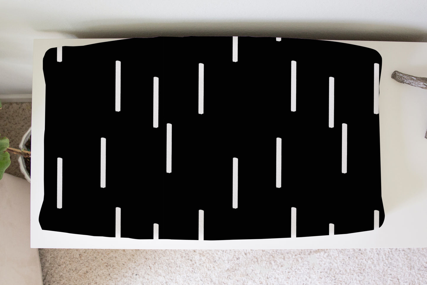 Black mud cloth dash pattern changing pad cover on white dresser in nursery setting