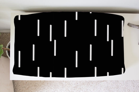 Black mud cloth dash pattern changing pad cover on white dresser in nursery setting