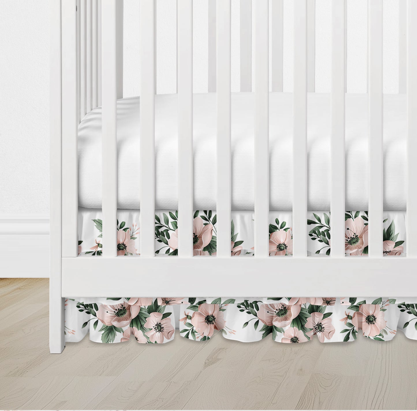 Ruffled crib skirt in blush pink floral pattern with greenery on white background