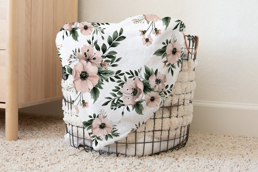 Blush and sage floral baby blanket with sherpa backing, featuring soft pink watercolor flowers and green leaves, styled in a cozy nursery basket