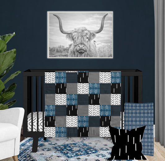 Mudcloth-inspired crib bedding set in black, white, gray, and navy with tribal patterns, displayed in a modern nursery.