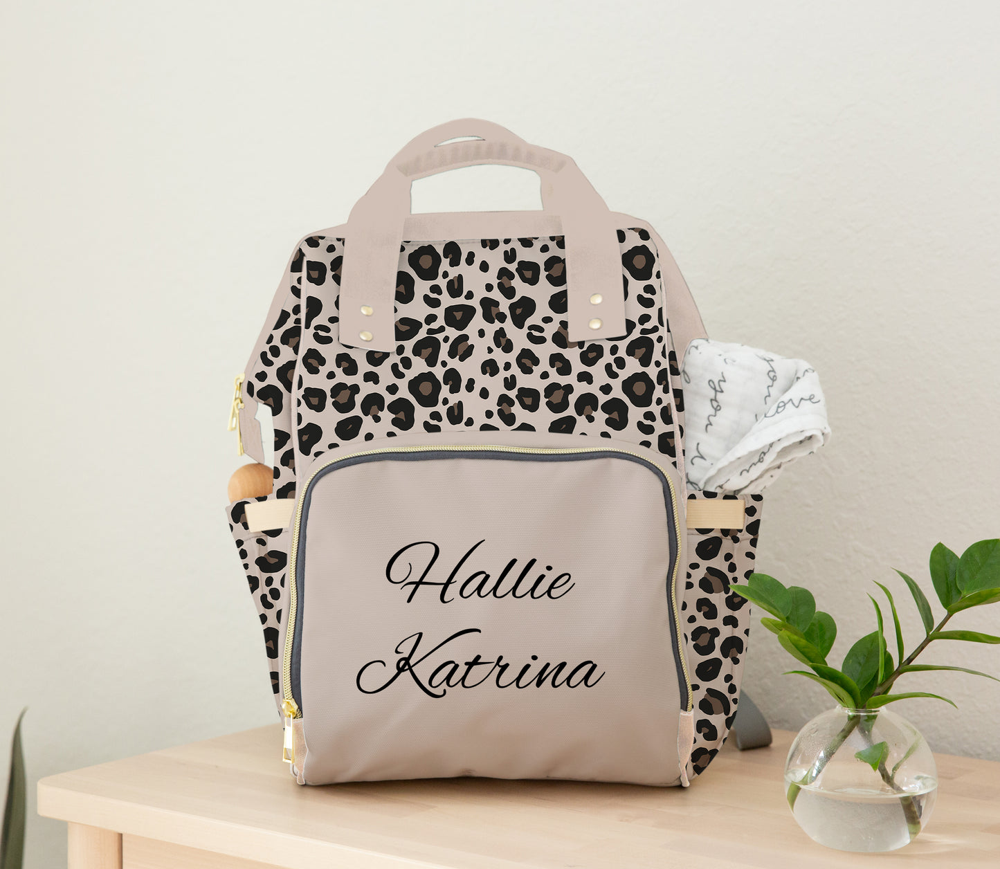 Personalized leopard print diaper bag backpack with custom name on front pocket, neutral beige accents, top handles, backpack straps, and side pockets.