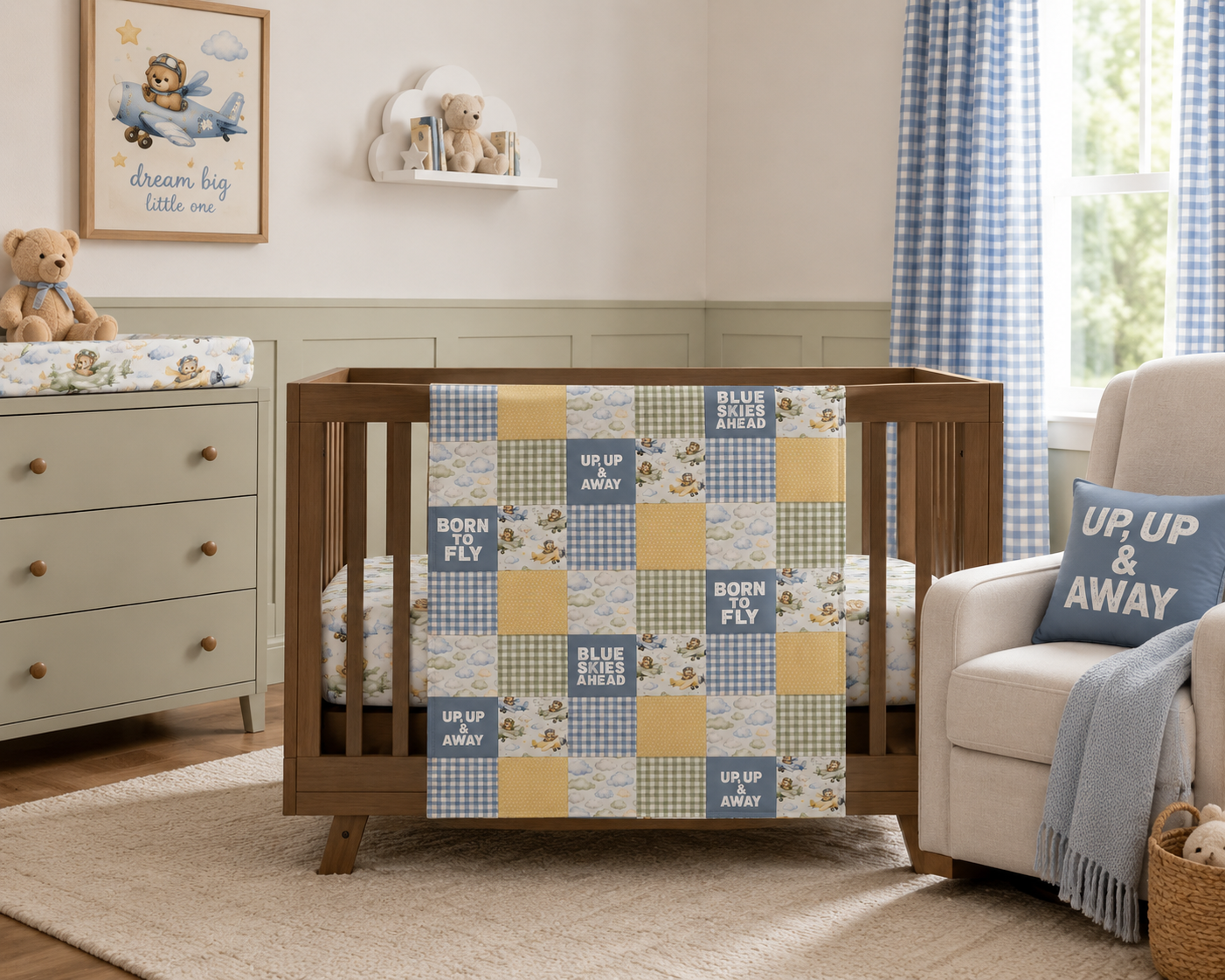 Airplane teddy bear patchwork baby blanket with blue gingham, sage green plaid, yellow accents, watercolor clouds, and minky backing hanging on a nursery crib.