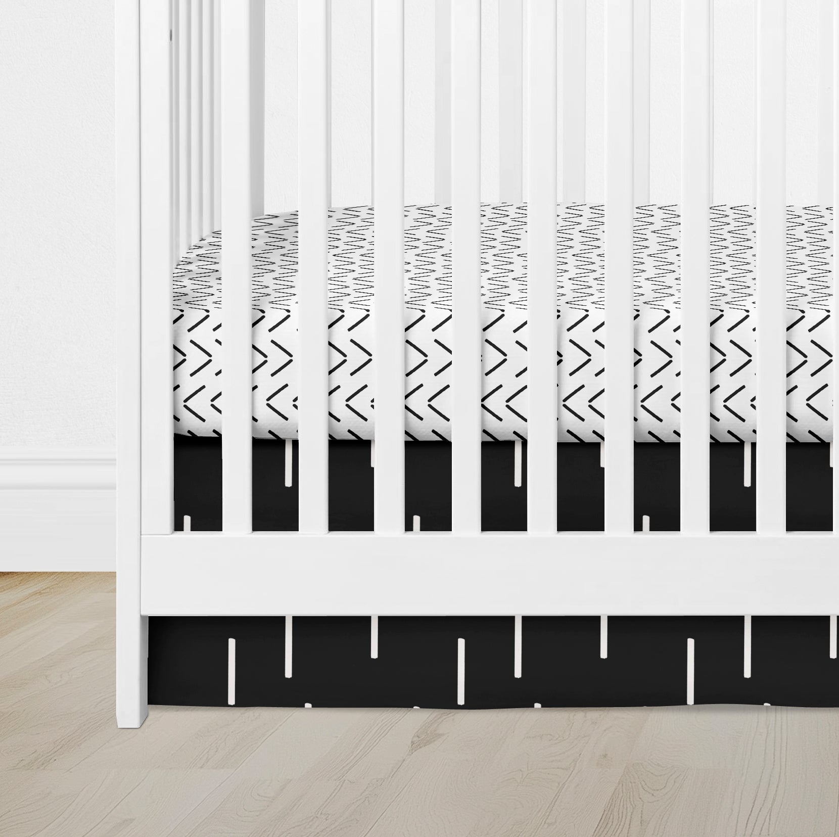 Black mud cloth crib skirt with white dash print in a white crib with matching sheet