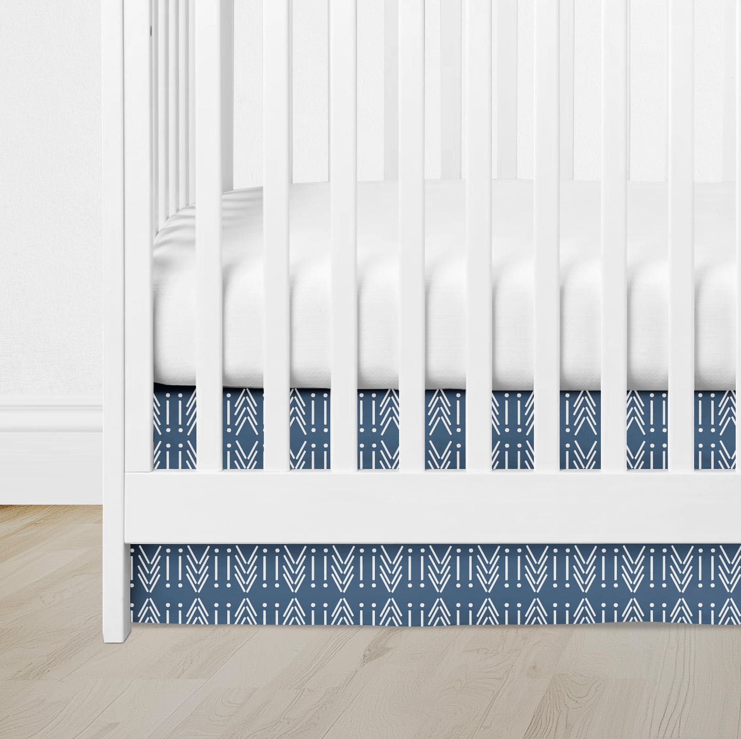 blue crib skirt with white mudcloth arrow pattern under white crib